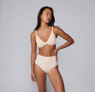 On a light gray studio backdrop, Amber wears the Bliss Highwaist in Rose with the Base Unlined Bra in Rose. Shown in a full-body view, the high-waisted underwear features a smooth waistband, full coverage, and soft microfiber fabric designed for comfortable, everyday wear with a no-show feel under clothing.