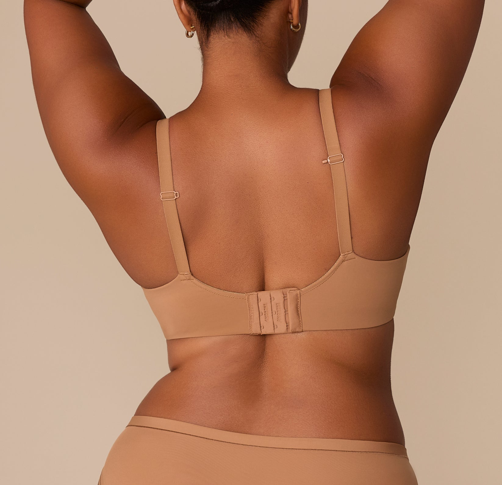 Back view of Zarria wearing the Base Wirefree T-Shirt Bra in Tan. The hook-and-eye closure and fully adjustable straps are shown, designed for everyday comfort and fit flexibility.