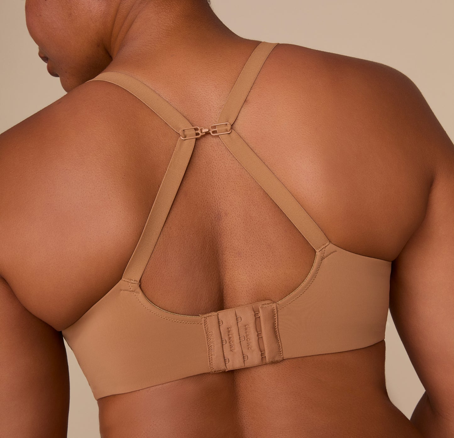 Zarria wearing the Base Wirefree T-Shirt Bra in Tan with straps converted into a racerback using the sliding J-hook. The image highlights the bra’s adjustable and versatile fit.