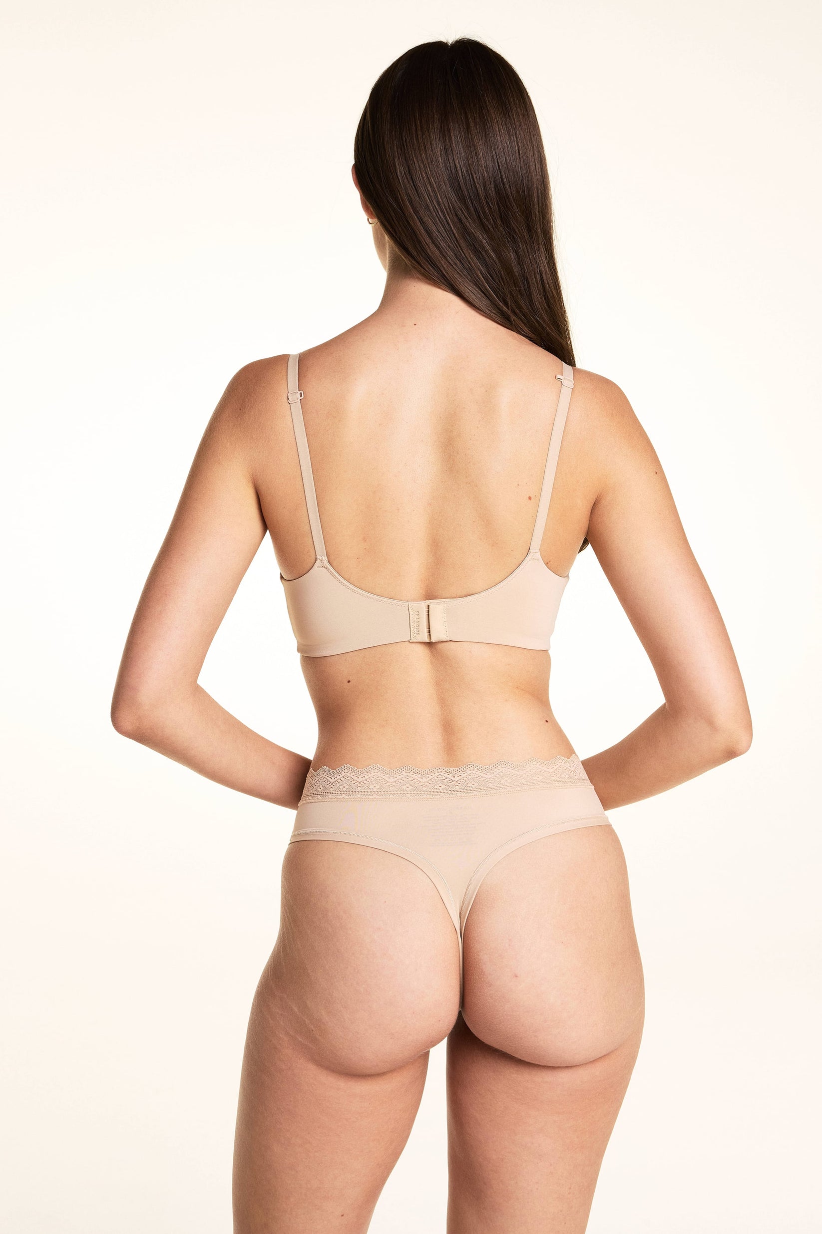 On a light studio backdrop, Laura wears the Base Wirefree Bra in Beige with matching underwear, shown from the back to highlight the smooth silhouette and lace waistband detail.