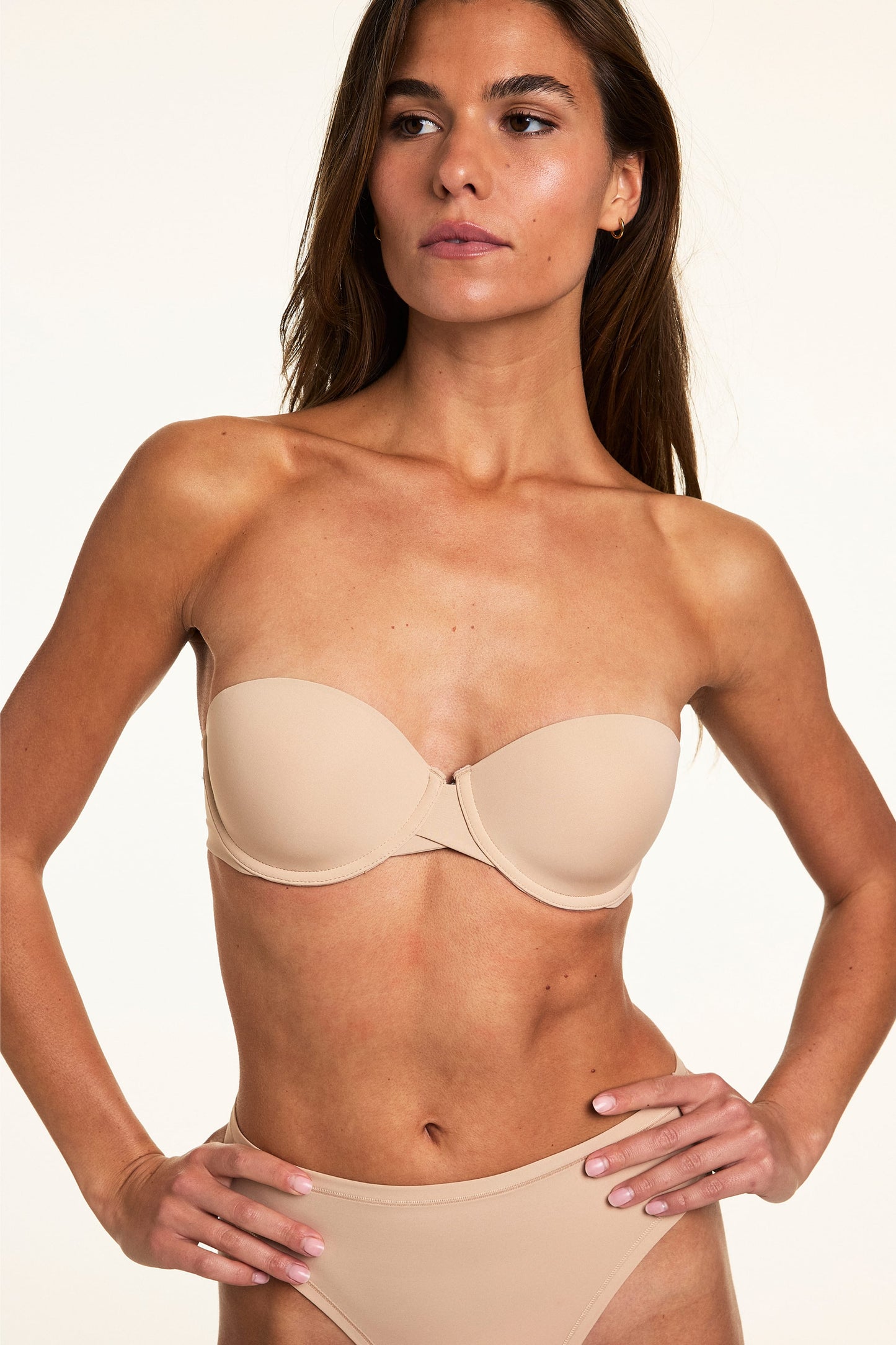 Against a neutral studio backdrop, Gianna wears the Base Strapless Bra in Beige with matching underwear, highlighting the lightly lined cups, underwire support, and smooth strapless design.
