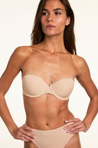 Against a neutral studio backdrop, Gianna wears the Base Strapless Bra in Beige with matching underwear, highlighting the lightly lined cups, underwire support, and smooth strapless design.