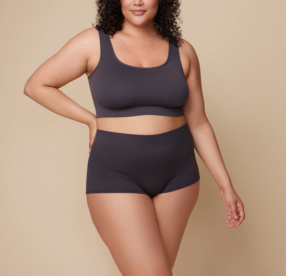 Bianca stands with her hands resting by her sides, wearing the Lounge Boyshort in Charcoal. The image highlights the comfortable fit and soft fabric of the boyshort. sizing: Bianca wears size 2XL