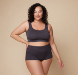 Bianca stands facing forward, wearing the Lounge Rib Scoop Bralette and Lounge Rib Boyshort in Charcoal. The scoop neckline and ribbed texture highlight the bralette’s comfortable fit. sizing: Bianca wears size 2XL