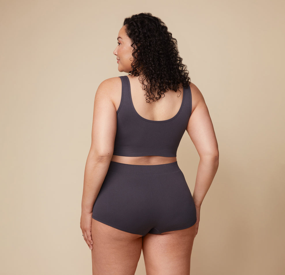 Bianca is turned to the side, showing the back of the Lounge Rib Scoop Bralette and Lounge Rib Boyshort in Charcoal. The seamless design offers full comfort and support.