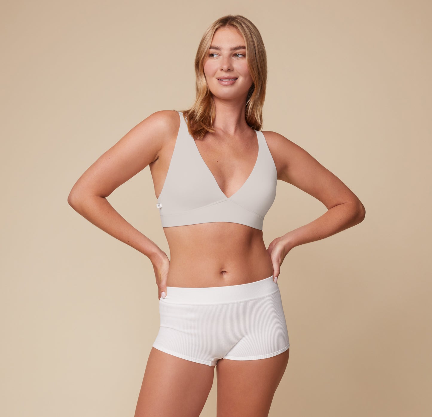 Megan smiling and wearing the Bliss Plunge Adjustable Bralette in Frost paired with the Lounge Rib Boyshort in White. The image showcases the bralette’s wireless comfort and sleek, everyday wearability.