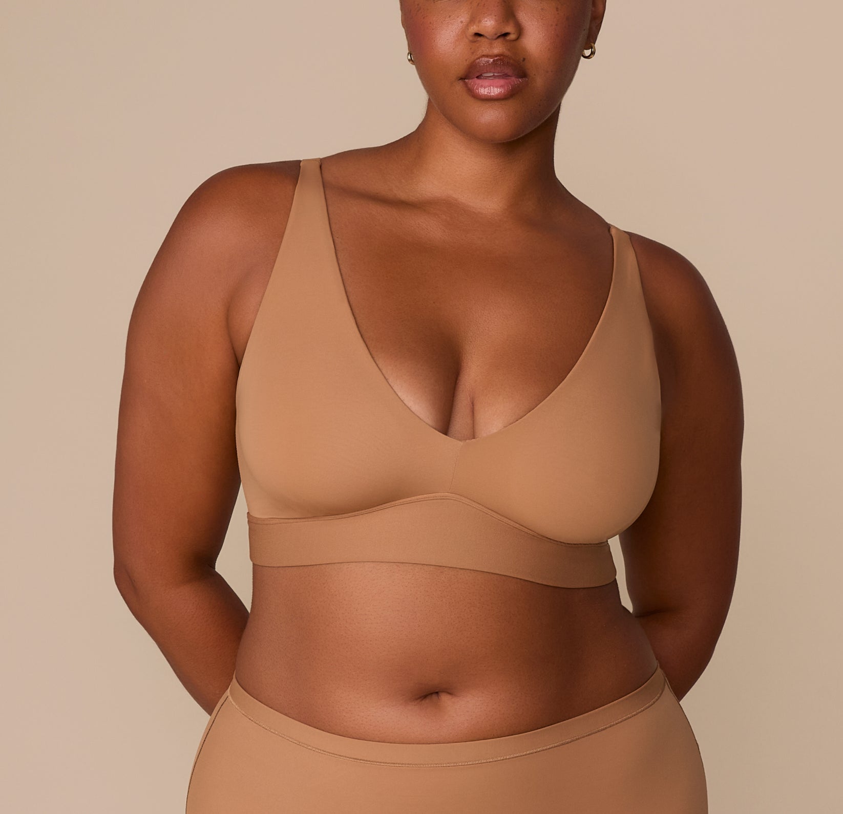 Front view of Zarria wearing the Bliss Plunge Adjustable Bralette in Tan, highlighting the deep V neckline and wide underband for support. sizing: Zarria wears size XL