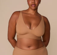 Front view of Zarria wearing the Bliss Plunge Adjustable Bralette in Tan, highlighting the deep V neckline and wide underband for support. sizing: Zarria wears size XL
