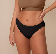 Close-up front view of Sonnie wearing the Bliss Bikini in Black and the Bliss Scoop Bralette in Brown. The bikini’s high-rise, mid-cut design offers moderate coverage and a smooth fit against the skin. sizing: Sonnie wears size Large
