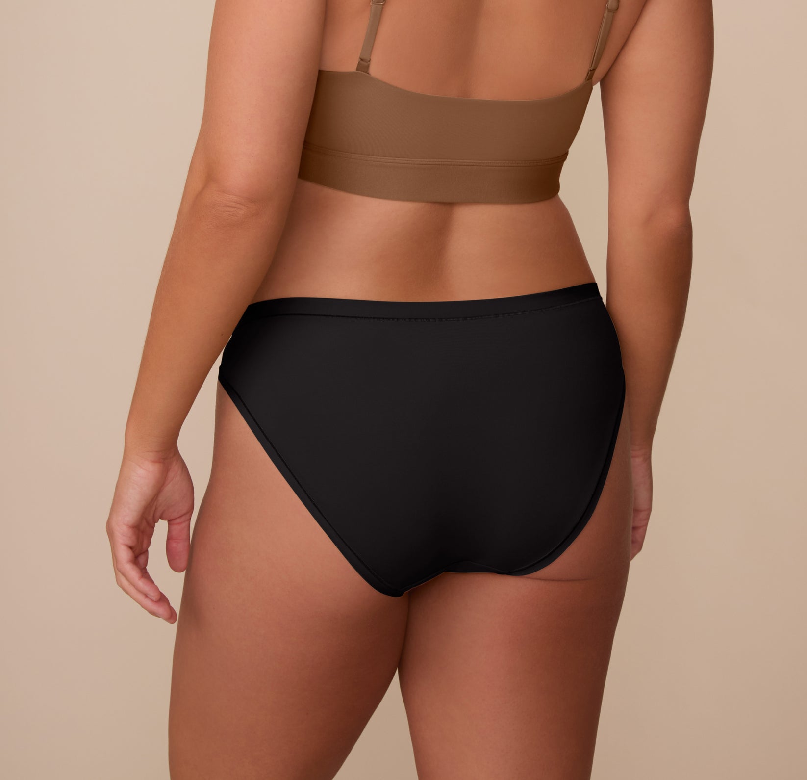 Back view of Sonnie in the Bliss Bikini in Black and Bliss Scoop Bralette in Brown. The image highlights the bikini’s full-coverage back and clean finish, ideal for no-show wear under clothing.