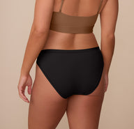 Back view of Sonnie in the Bliss Bikini in Black and Bliss Scoop Bralette in Brown. The image highlights the bikini’s full-coverage back and clean finish, ideal for no-show wear under clothing.