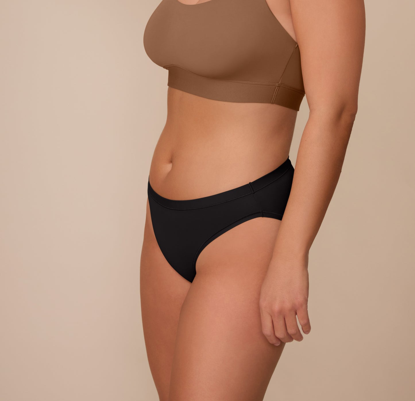 Side profile of Sonnie in the Bliss Bikini in Black and Bliss Scoop Bralette in Brown. The angle showcases the curve-hugging cut and elastic-free waistband of the bikini for all-day comfort.
