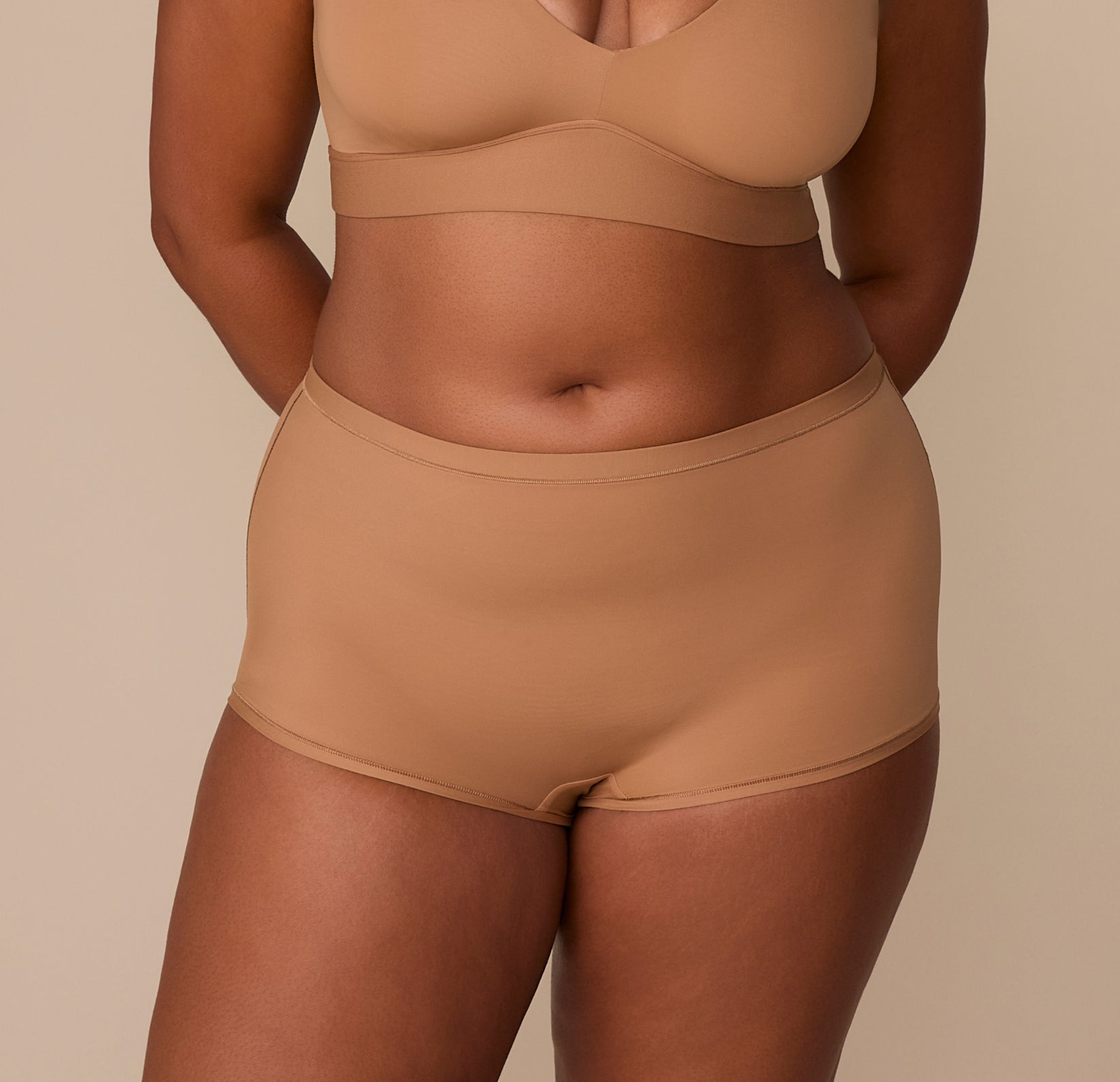 Front view of Zarria wearing the Bliss Boyshort in Tan. The high-rise fit and smooth waistband offer full coverage and a seamless silhouette under clothing. sizing: Zarria wears size XL