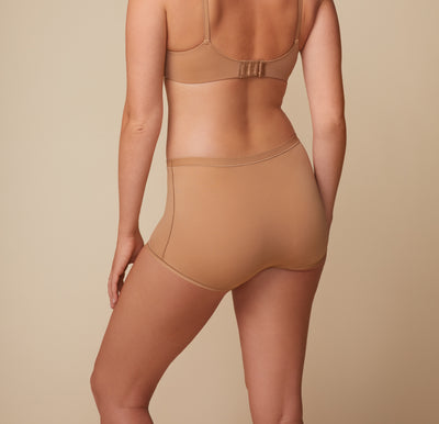 Back angle of Megan in the Bliss Boyshort in Tan. The shot captures the full back coverage and soft, second-skin fit across the hips.