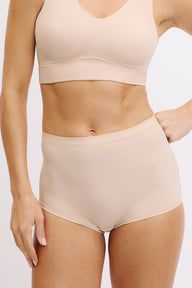 On a white studio backdrop, Darion wears the Bliss Boyshort in Beige, showing the high-rise waist, smooth microfiber fabric, and full front coverage with a clean, elastic-free finish. sizing: Darion wears size Small