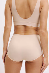 On a white studio backdrop, Darion wears the Bliss Boyshort in Beige from the back, highlighting the high-rise fit, smooth waistband, and full back coverage designed to sit flat under clothing.