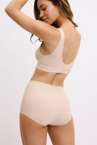 On a white studio backdrop, Darion is shown from a side-back angle wearing the Bliss Boyshort in Beige, featuring the soft microfiber fabric, high waist, and clean edges along the leg opening.