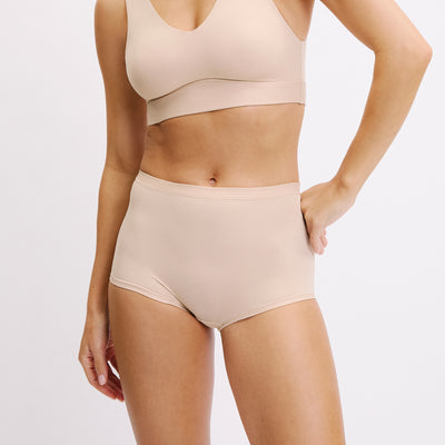 On a white studio backdrop, Darion wears the Bliss Boyshort in Beige from a front angle, highlighting the smooth waistband, high-rise coverage, and soft microfiber fabric.