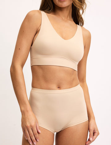 On a light studio backdrop, Darion wears the Bliss Scoop Bralette and Bliss Boyshort in Beige, featuring a scoop neckline, wide underband, and full coverage fit. sizing: Darion wears size Small