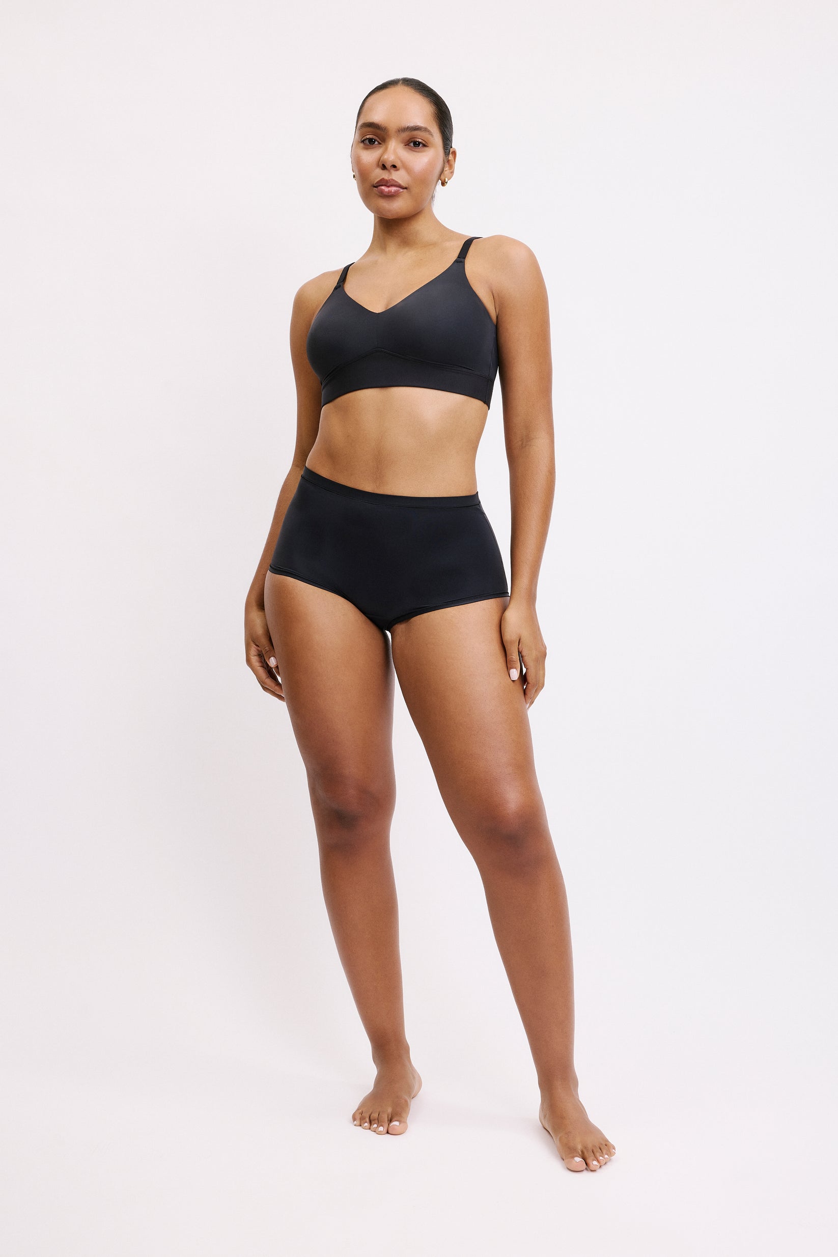 On a white studio backdrop, Amber stands facing forward wearing the Bliss Boyshort in Black, showing the mid-rise fit, soft microfiber fabric, and comfortable boyshort silhouette designed for everyday wear.