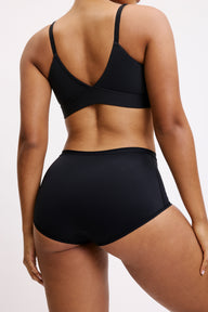 On a white studio backdrop, Amber is shown from behind wearing the Bliss Boyshort in Black with the matching Bliss bralette, highlighting the full back coverage, wide waistband, and smooth microfiber fabric with a no-show look.
