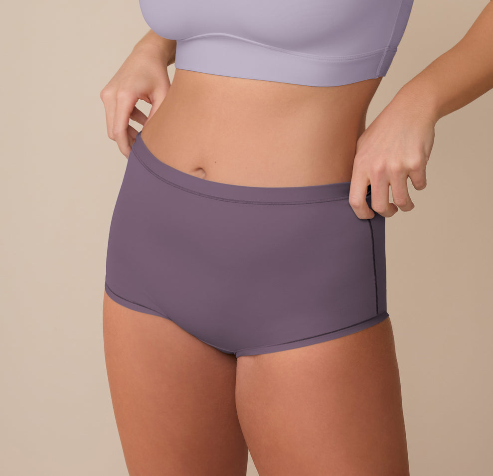 Sonnie adjusts the waistband of the Bliss Boyshort in Eclipse while wearing the Bliss Bralette in Violet. This side angle highlights the boyshort’s flexible stretch and the bralette’s soft, supportive underband.
