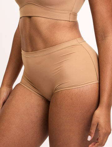 On a light studio backdrop, Amber wears the Bliss Boyshort in Tan with a matching Bliss bralette. The high-rise boyshort features soft microfiber fabric with smooth, elastic-free edges and full back coverage.  