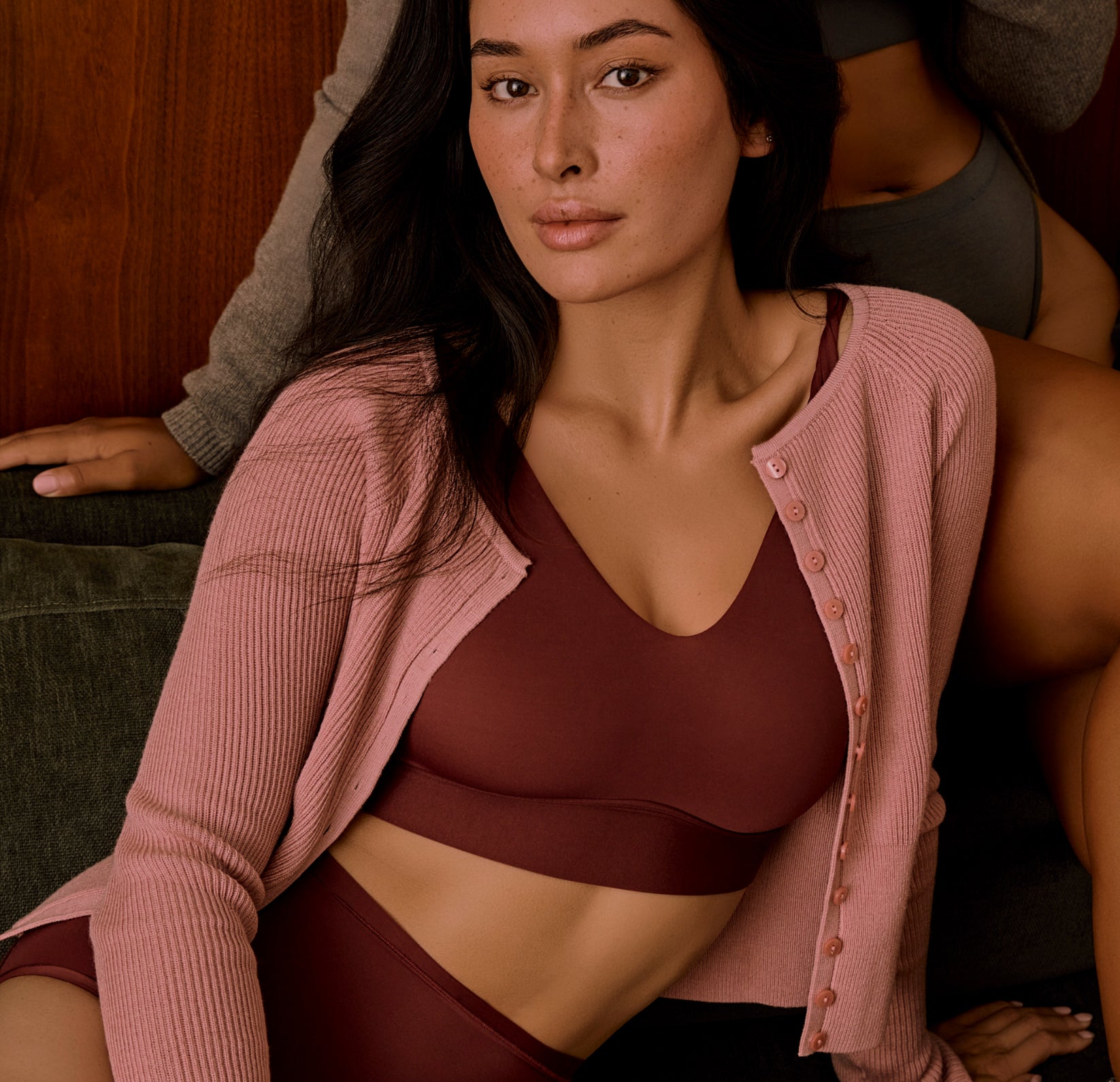 A model wears the Bliss Bralette and Bliss Highwaist Brief in Bordeaux, layered under a soft pink cardigan. The image showcases the wireless support and ultra-soft feel of the matching set.