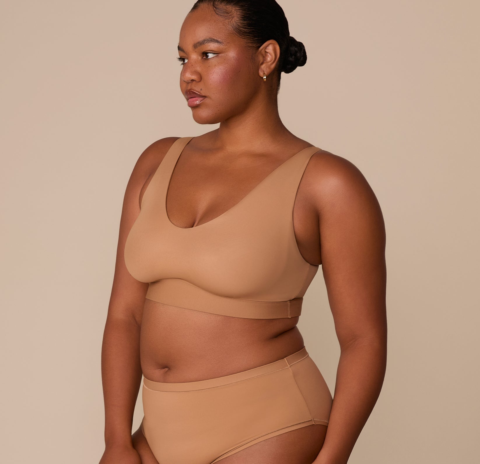 Zarria in a relaxed three-quarter pose wearing the Bliss Bralette in Tan, showing the curve-hugging fit and extended band.