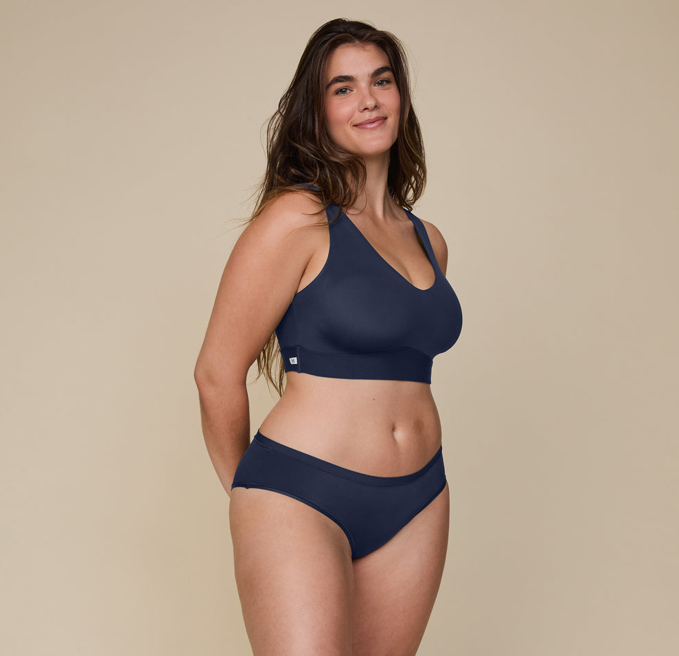 Summerlyn poses at a three quarter angle wearing the Bliss Bralette in the color True Blue with the Bliss Hiphugger underwear. 