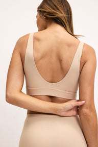 From the back on a light studio backdrop, Darion wears the Bliss Bralette in Beige, showing the scoop back design, wireless band, and smooth microfiber fabric.