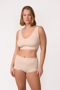 On a light neutral studio backdrop, Sonny wears the Bliss Bralette in Beige with matching underwear, shown in a full-body view. The pullover bralette has a scoop neckline and wireless band designed for soft, all-day support.