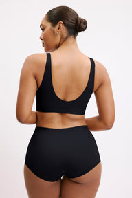 On a light neutral studio backdrop, Amber wears the Bliss Bralette in Black, shown from the back. The wide straps and scoop back provide soft support with a smooth, flexible band.