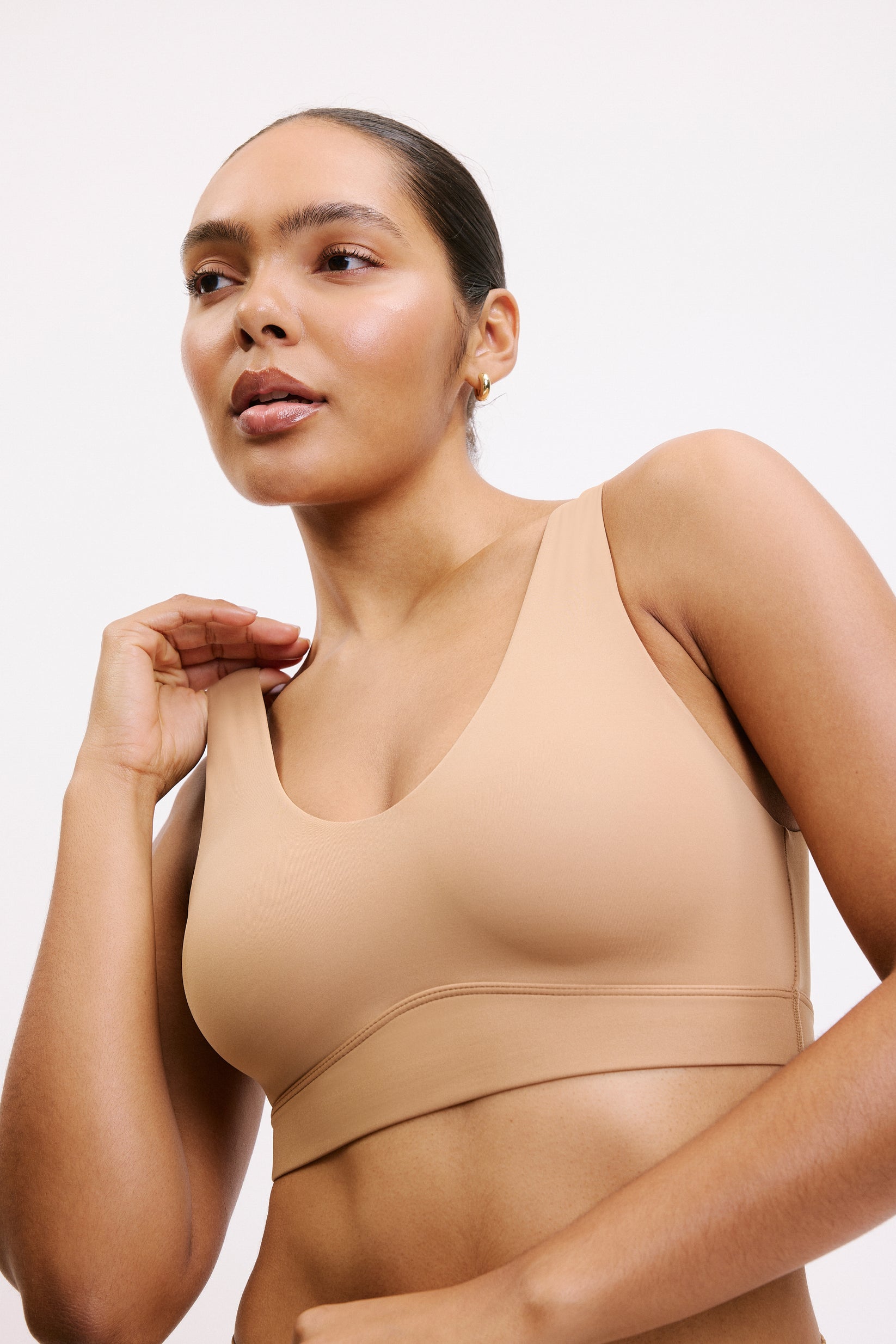 On a white studio backdrop, Amber wears the Bliss Bralette in Tan, shown in a close-up three-quarter front view. The scoop neckline, smooth underband, and soft microfiber fabric are visible.