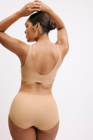 On a white studio backdrop, Amber is shown from the back wearing the Bliss Bralette in Tan with the matching high-rise brief, highlighting the wide straps, smooth back band, and clean, wire-free construction.