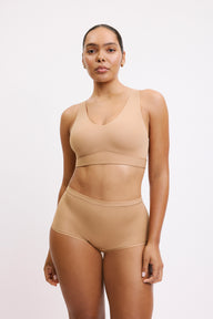 On a white studio backdrop, Amber is shown in a full-body front view wearing the Bliss Bralette in Tan with the matching high-rise brief, highlighting the wireless design, smooth underband, and comfortable everyday silhouette.