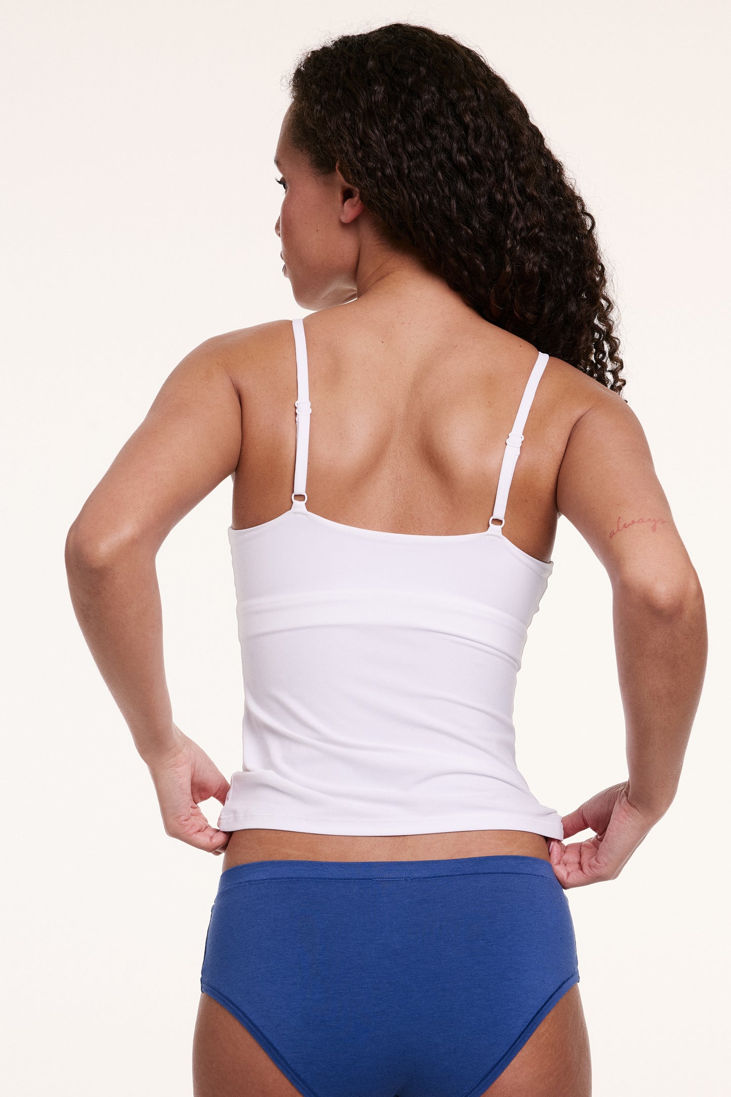Shown from the back in a studio setting, Courtney wears the Bliss Cami in White. The thin adjustable straps and smooth, stretchy microfiber fabric create a flexible, stay-put fit.