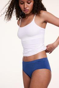 Shown from a slight side angle in a studio setting, Courtney wears the Bliss Cami in White with blue underwear. The smooth, stretchy microfiber fabric and thin adjustable straps provide flexible, everyday comfort.