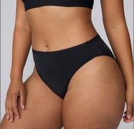 On a light gray studio backdrop, a close-up side view of India wearing the Bliss French Cut Brief in Black highlights the smooth waistband and high-cut leg shape.