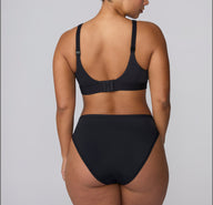 On a light gray studio backdrop, India is shown from behind wearing the Bliss French Cut Brief in Black with the matching bra, highlighting the smooth back coverage and minimal stitching.