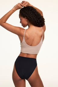 From the back on a light studio backdrop, Courtney wears the Bliss French Cut in Black with a beige bralette. The underwear features a high-cut leg, smooth microfiber fabric, and moderate back coverage.