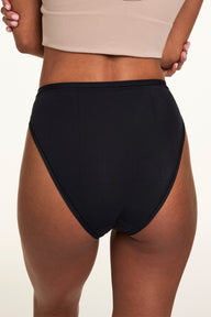 Close-up back view on a light studio backdrop, Courtney wears the Bliss French Cut in Black with a beige bralette. The underwear features smooth microfiber fabric and moderate back coverage with a high-cut leg.