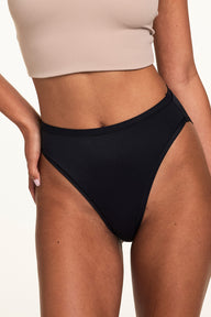 Close-up front view on a light studio backdrop, Courtney wears the Bliss French Cut in Black with a beige bralette. The underwear features a high-rise fit, smooth microfiber fabric, and high-cut leg openings.