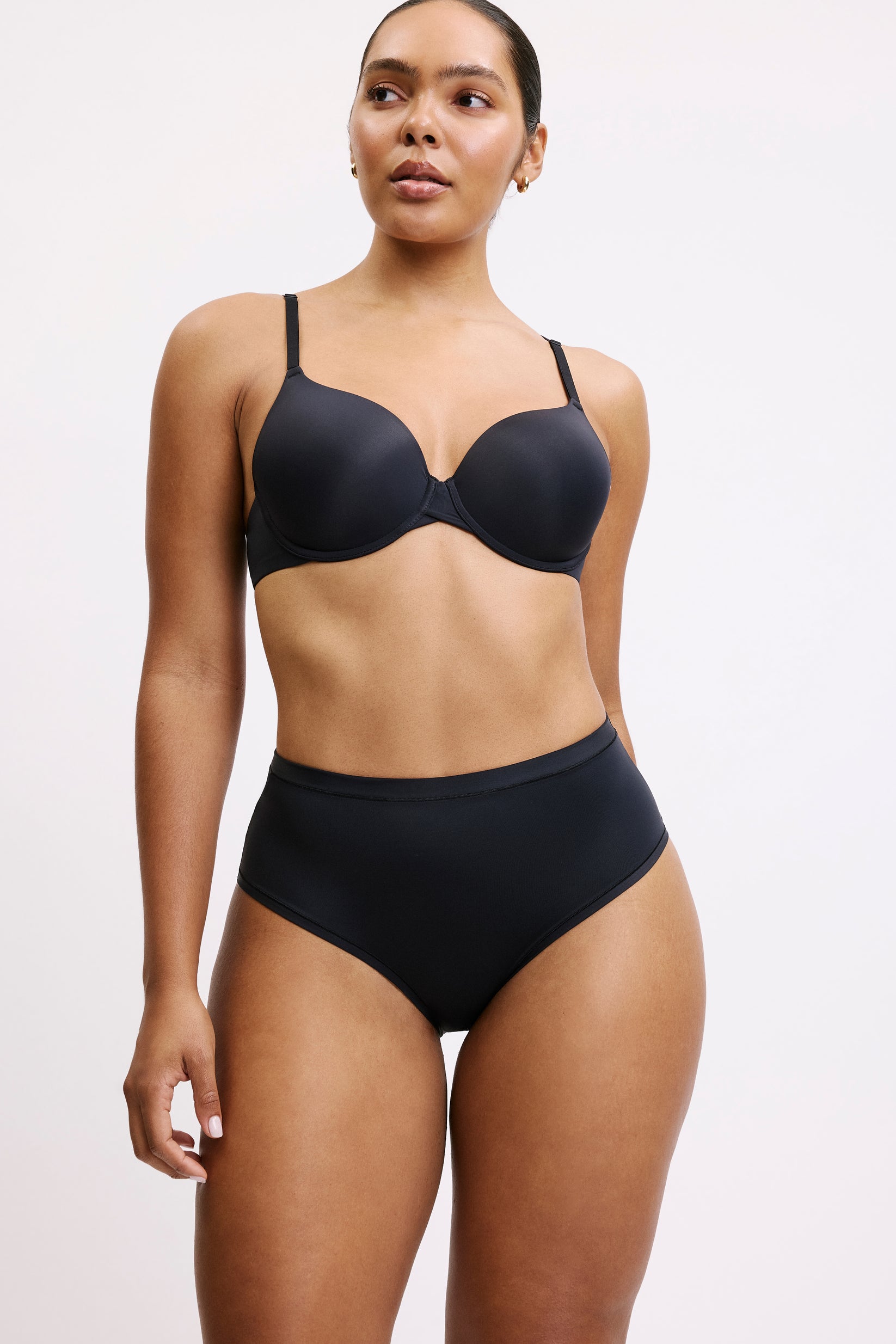 On a light grey studio backdrop, Amber wears the Bliss Highwaist in Black, front view. The high-rise silhouette sits smoothly at the waist with full coverage through the front, made from ultra-soft microfiber fabric designed to feel barely there. sizing: Amber wears size Large