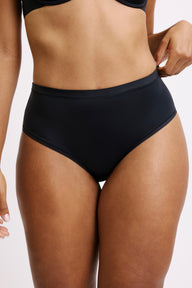 Close-up on a light grey studio backdrop of Amber wearing the Bliss Highwaist in Black. The smooth waistband sits comfortably at the natural waist, showcasing the soft, breathable microfiber fabric and clean, no-show finish.