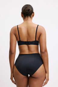 On a light grey studio backdrop, back view of Amber wearing the Bliss Highwaist in Black paired with a matching black bra. The high-waisted silhouette offers full coverage with smoothing microfiber fabric designed to disappear under clothing.