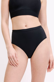 On a white studio backdrop, a front close-up shows Megan wearing the Bliss Highwaist Brief in Black. The smooth waistband and full front coverage are visible, designed to sit comfortably at the waist. sizing: Megan wears size Small