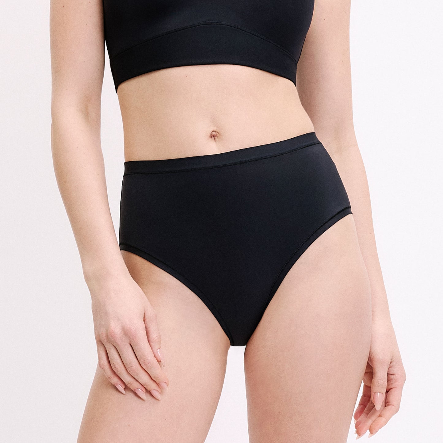 On a white studio backdrop, a straight-on front view shows Megan wearing the Bliss Highwaist Brief in Black. The soft microfiber fabric and clean leg openings are visible for everyday comfort.