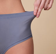 A close-up of Gracie pulling the waistband slightly to showcase the soft, flexible fabric that offers a secure yet comfortable fit.
