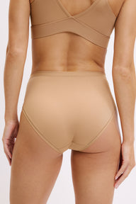 On a white studio backdrop, Darion is shown in a close-up back view wearing the Bliss Triangle Bralette and Bliss Highwaist Brief in Tan, showing the bralette’s supportive back band and the brief’s full back coverage with a smooth, elastic-free finish.
